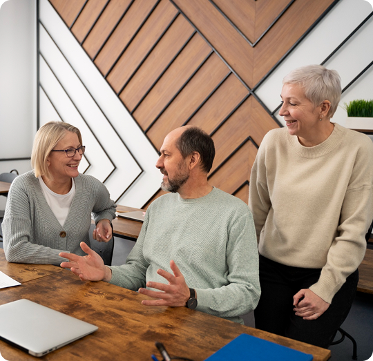 Group of three adults engaged in a discussion at a wooden table, emphasizing collaboration and community in estate planning education.
